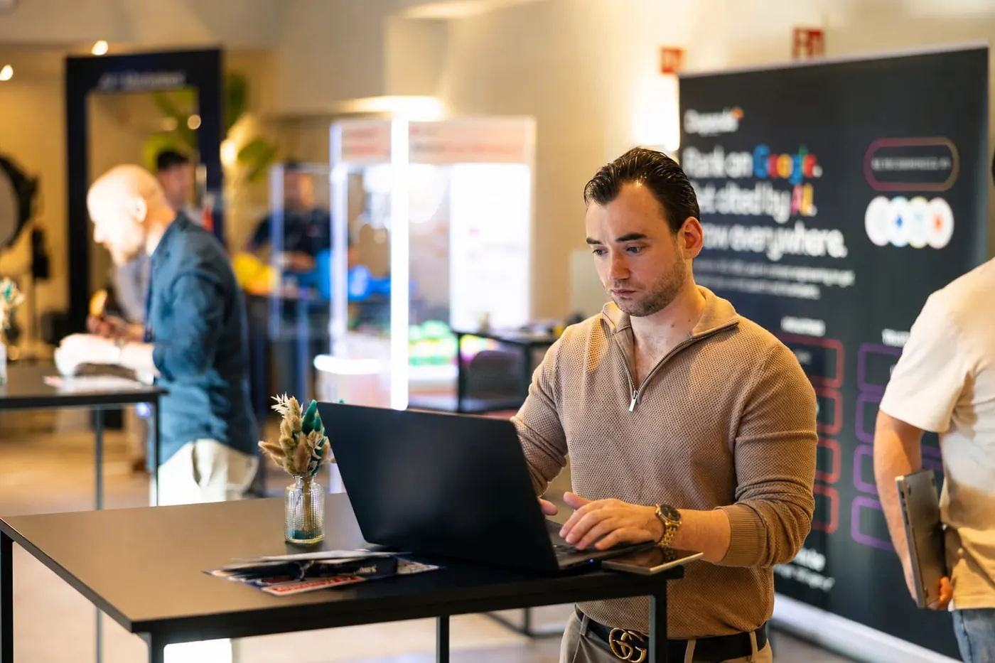 Toon Rombaut aan het werk op een netwerkevent, met een banner over hoger scoren in Google en in AI
